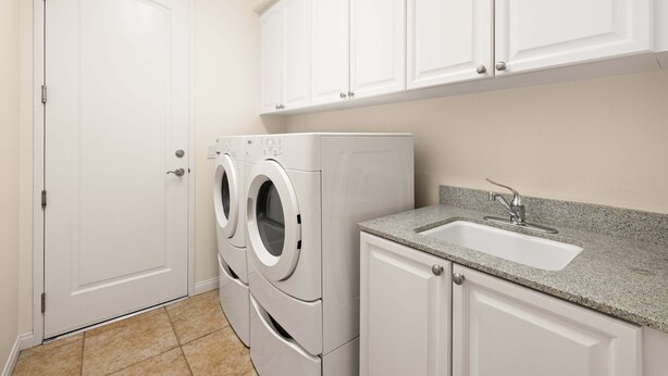 A laundry room with a front-loading washer and dryer, a sink with a granite countertop, and white cabinetry. - Family Friendly Legacy Villas Retreat- Mountain Views (La Quinta)