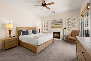 Une chambre à coucher comprenant un lit, des tables de chevet, une chaise, une cheminée et un ventilateur de plafond.