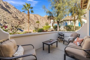 A balcony with outdoor furniture, a small table, and a view of a mountainous landscape.