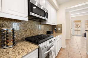 A kitchen with granite countertops, stainless steel appliances, and white cabinetry. - Family Friendly Legacy Villas Retreat- Mountain Views (La Quinta)