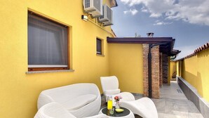 A yellow exterior wall with air conditioning units, a window with a curtain, and a seating area with white chairs and a round table with a glass and a vase. - Villa Ambrosiana (74204-K1) - Vodnjan (Vodnjan)