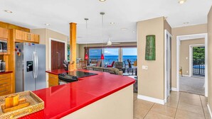 Et moderne køkken med rødt bordplade, rustfrie stål hvidevarer og udsigt til en balkon med udendørs møbler.