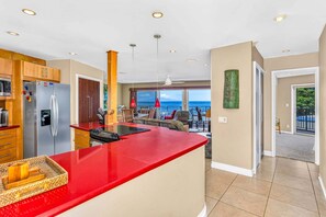 Eine moderne Küche mit roter Arbeitsplatte, Edelstahlgeräten und Blick auf einen Balkon mit Sitzgelegenheit.