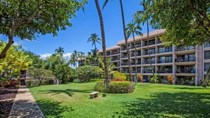 A hotel with multiple balconies, lush green lawns, and palm trees. - Budget Friendly - Kihei Akahi C-608, Ocean Views, Short Walk to Kamaole Beach II (Kihei)