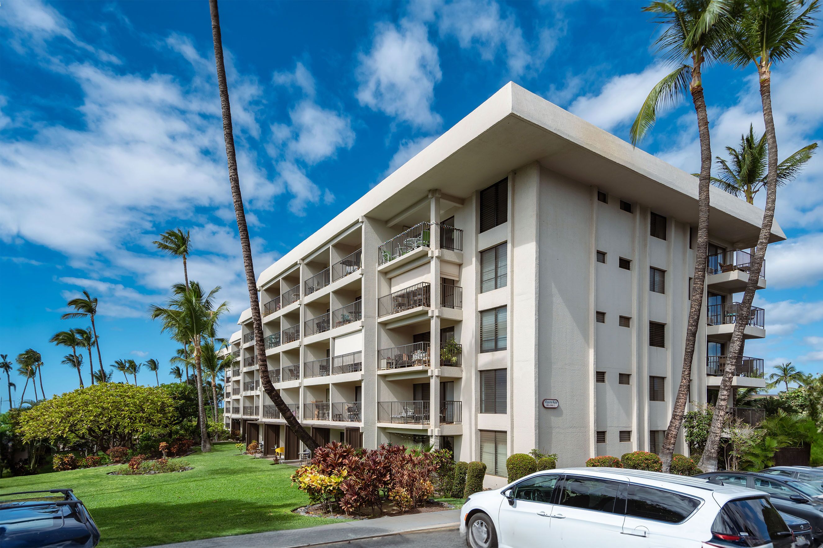 A multi-story hotel with balconies, surrounded by palm trees and a well-maintained lawn.