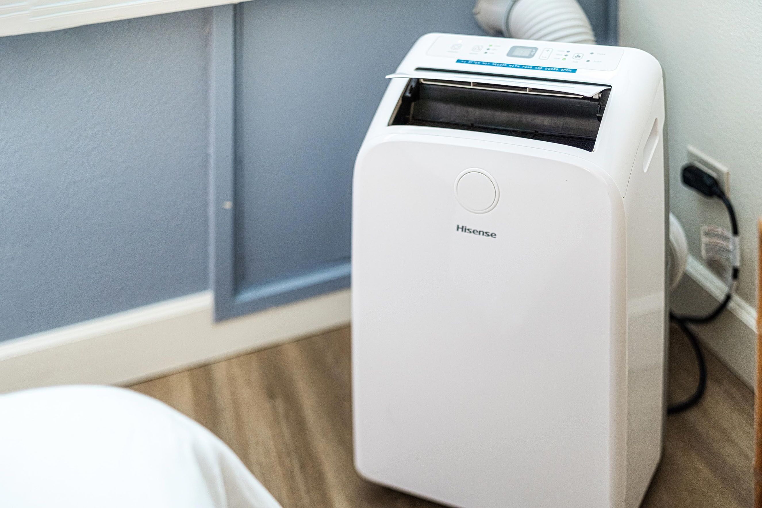A white Hisense air purifier in a room with a grey wall and wooden flooring.