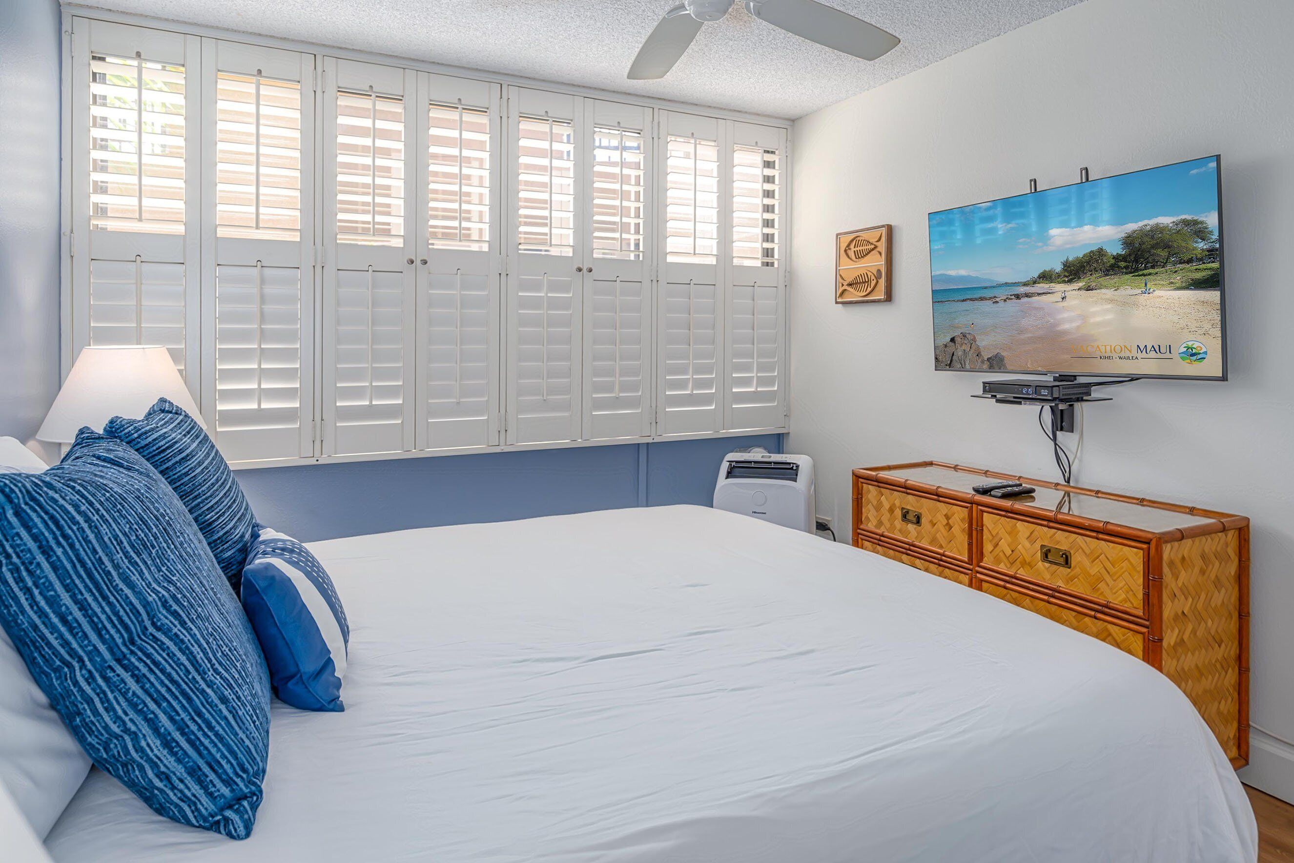 A bedroom with a bed, a television, a window with shutters, and a wooden dresser.