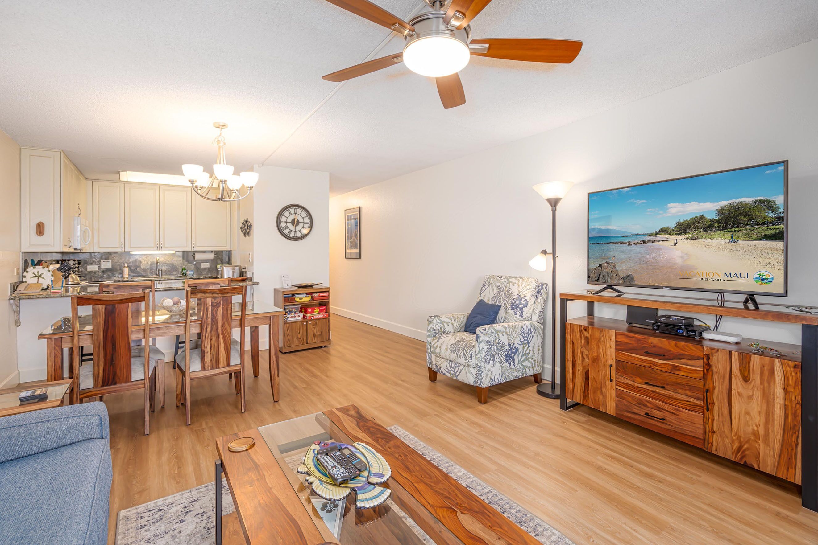 A spacious living area with a dining table, chairs, a sofa, a coffee table, a TV, and a ceiling fan.