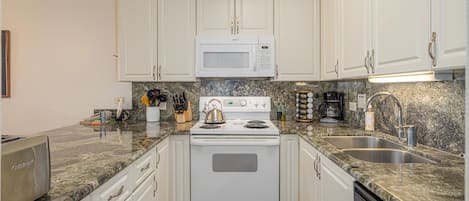 A kitchen with white cabinets, a white stove, a microwave, a sink, and granite countertops.