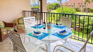 Un comedor con una mesa redonda dispuesta para cuatro personas, rodeada de sillas blancas, en un balcón con vistas a un campo de golf y edificios.