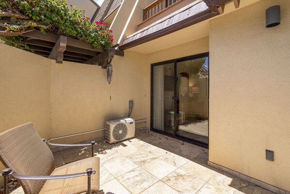 A small patio area with a chair, an air conditioning unit, and a sliding glass door leading to an interior space. - Maui Kamaole J-104 - Renovated, Private Ground Floor Unit, Two Lanais, Split AC! (Kihei)