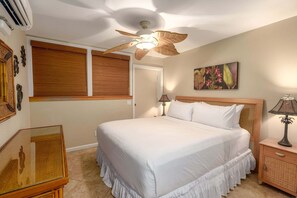Quarto com cama, ventoinha no teto, mesa de cabeceira, abajur e um quadro na parede.
