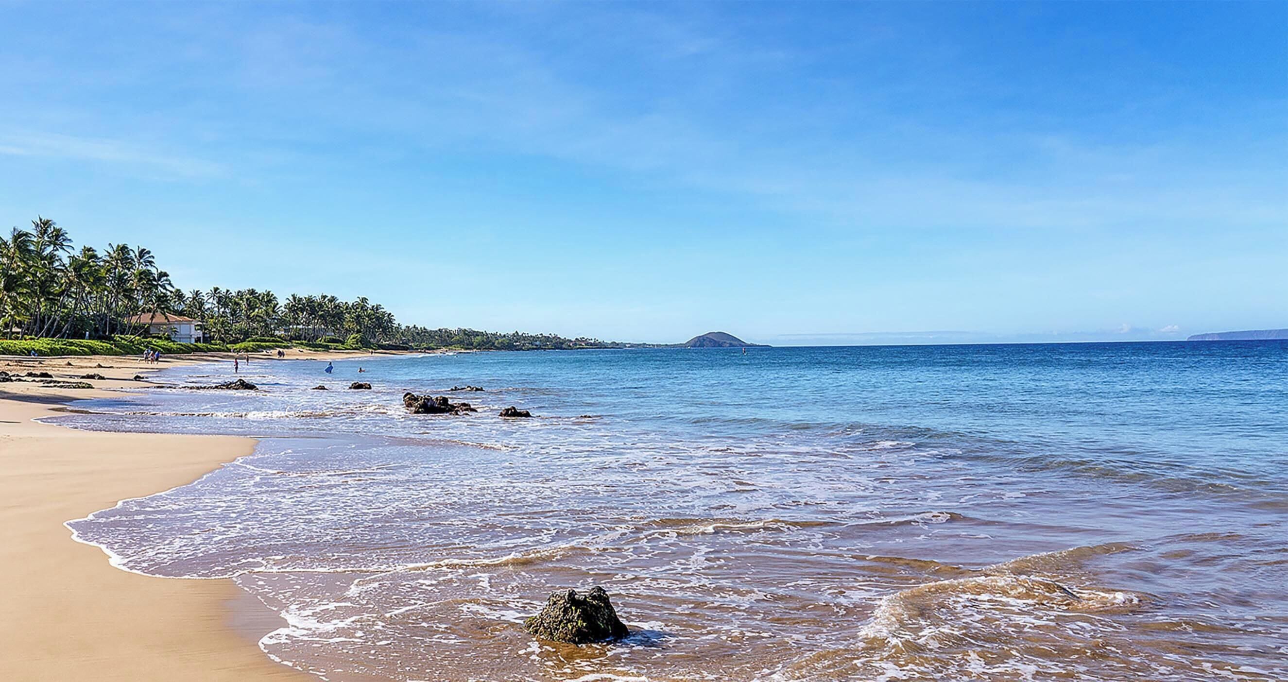 Une plage avec un ciel dégagé, une eau calme et une île qui se profile à l’horizon.