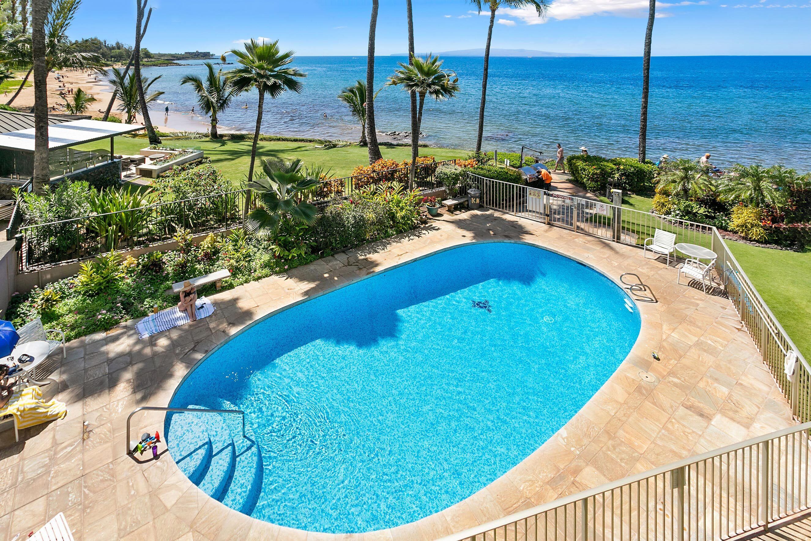 A swimming pool with a curved edge, surrounded by a patio area with lounge chairs and a view of the beach and ocean.