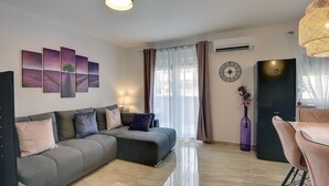 Een moderne woonkamer met een grijze bank, een eethoek met een stoel, een zwarte koelkast en een wandklok.