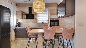 Een moderne keuken met een centraal eiland, hanglampen en een eethoek met barkrukken.