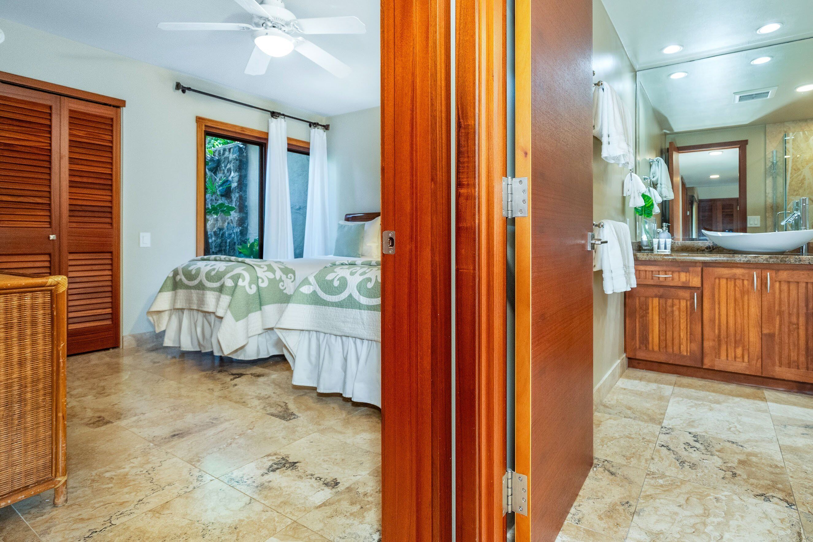A hotel room with a bed, a wooden wardrobe, a bathroom with a sink and mirror, and a ceiling fan.