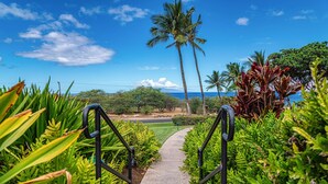 A pathway leading to a scenic view with palm trees and a clear sky. - Maui Kamaole G-202 - Spectacular Views, Updated and Elegant, Wi-fi & Split-ac! (Kihei)