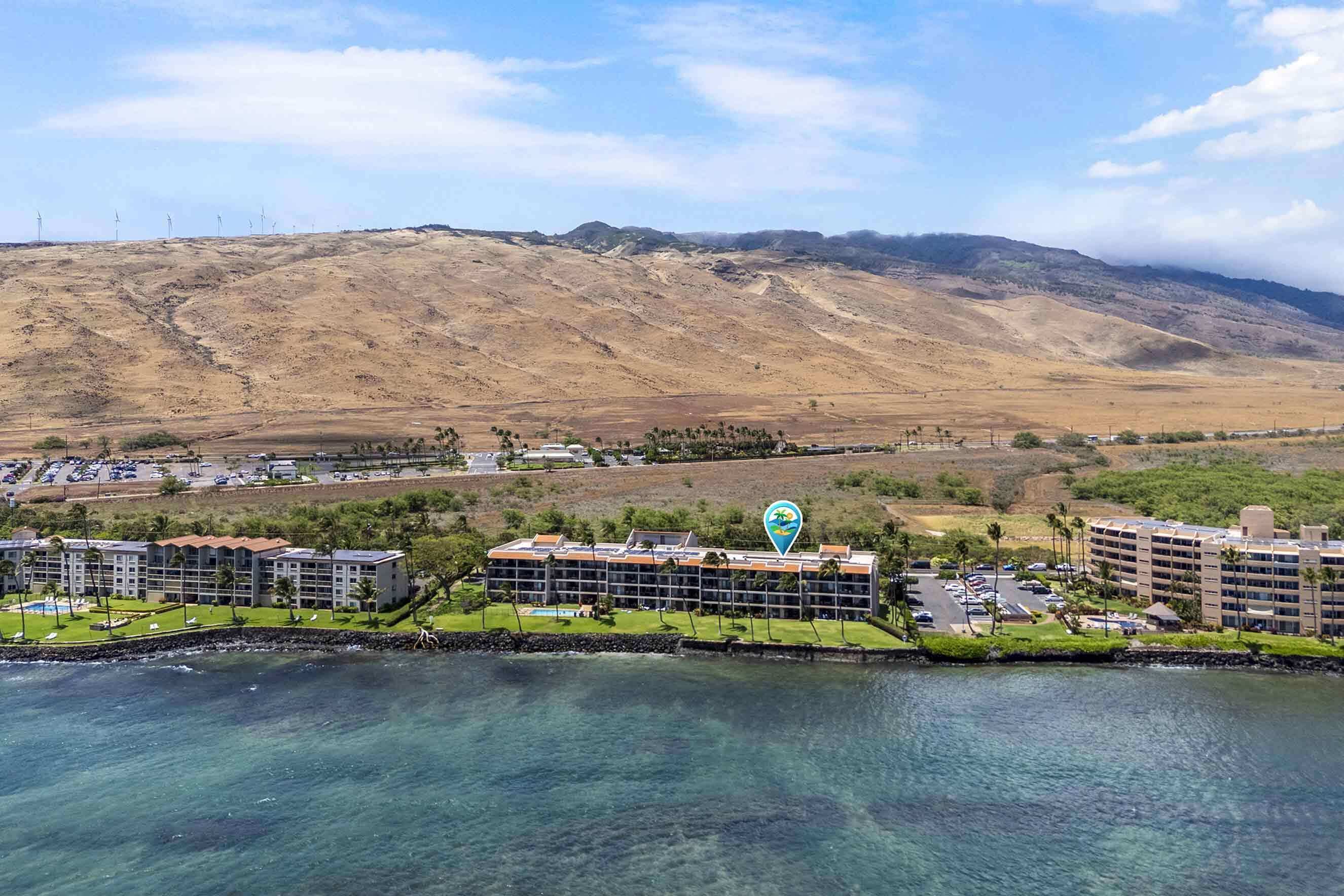 Un hotel costero con varias edificaciones, vistas despejadas al océano y montañas al fondo.