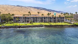 A hotel with a pool, palm trees, and a view of mountains. - Lauloa 410 - Top Floor, Oceanfront Lanai, Molokini & Halaeakala Views, Split A/C (Wailuku)