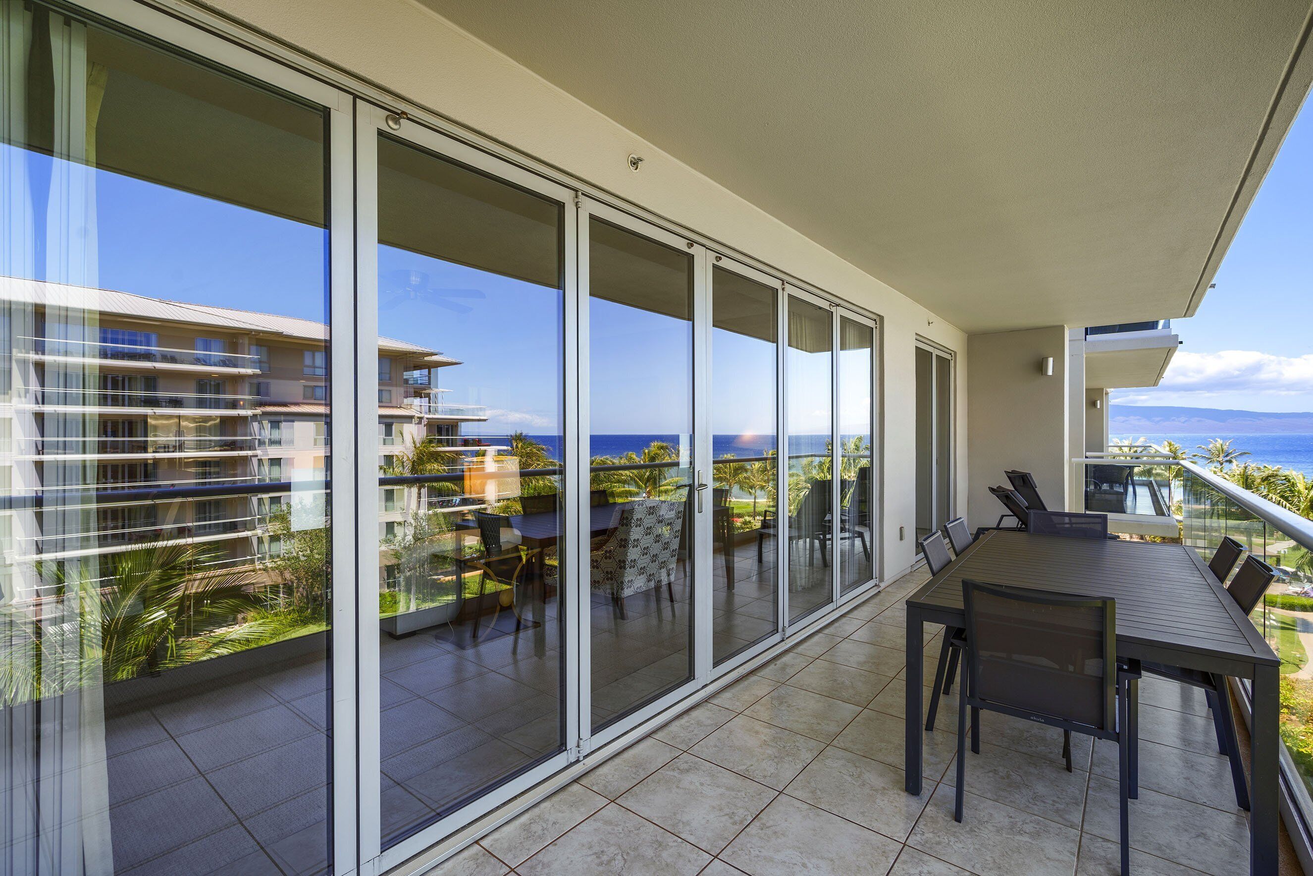 A balcony with a dining table and chairs, large sliding glass doors, and a view of the ocean and buildings.