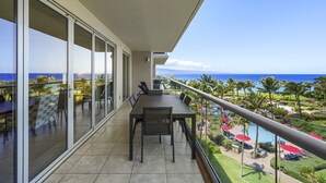 A balcony with a dining table and chairs, overlooking a pool and tropical landscape. - Honua Kai Resort Konea 505 Ocean & Sunset View 2BR at Kaanapali (Lahaina)