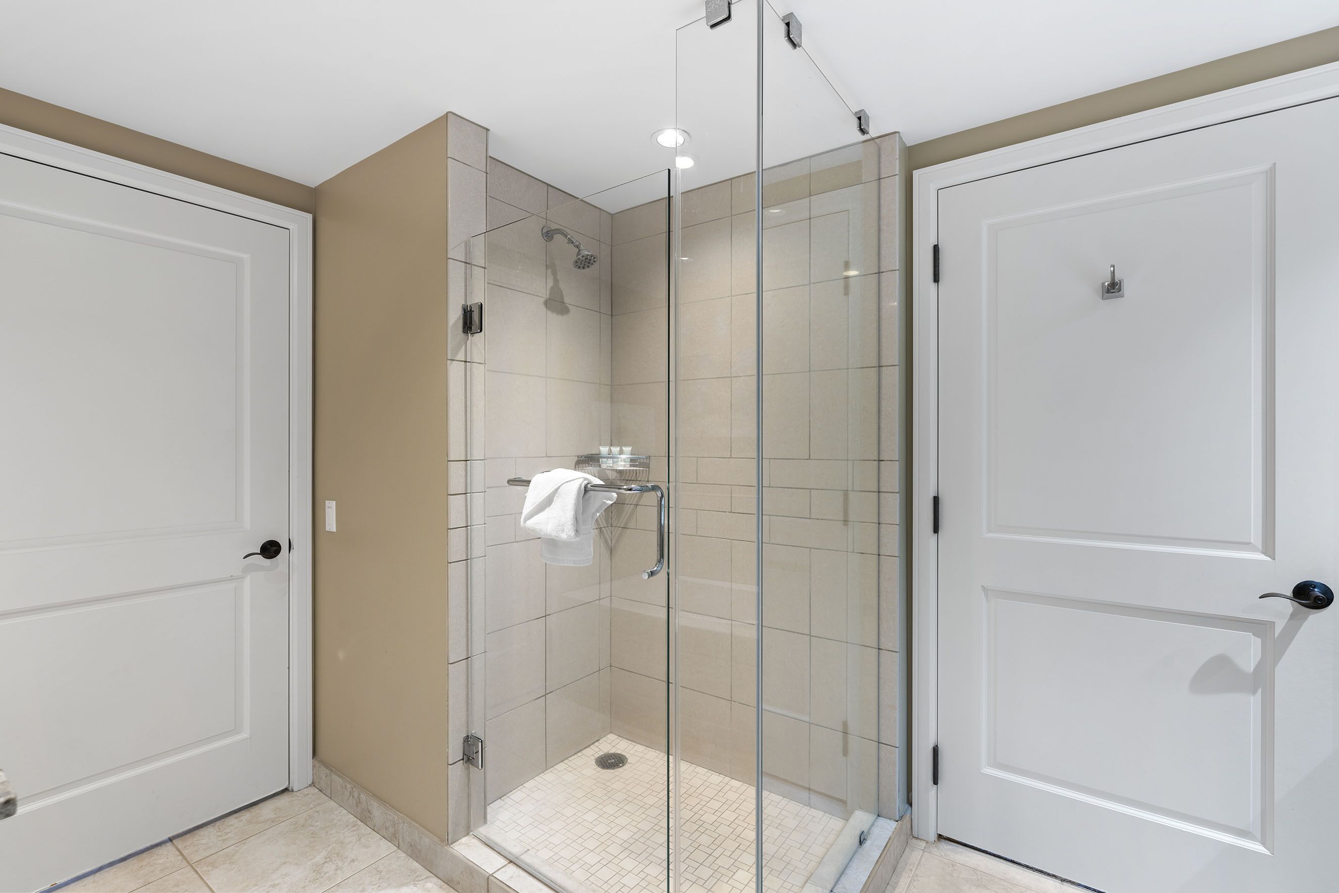 A modern bathroom with a glass-enclosed shower, white tiled walls, and a beige accent wall.