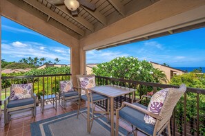 A covered outdoor seating area with a table and chairs, overlooking a lush garden and ocean view. - Discover Wailea Ekahi 39E - Breathtaking Ocean Views, Renovated, Wi-fi, Split AC (Kihei)