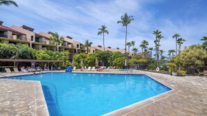 Une piscine entourée de chaises longues et de palmiers, le tout bordé d’un bâtiment doté de balcons.