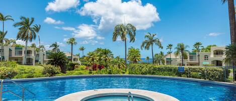 Una piscina con jacuzzi, rodeada de palmeras y un cielo azul despejado.