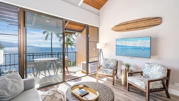 A spacious living area with a balcony, a round coffee table, two armchairs, and a television mounted on the wall.