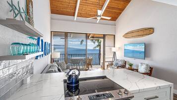 A modern kitchen with a large island, a ceiling fan, and a view of the ocean through large windows.