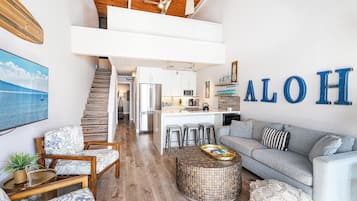 A spacious living area with a high ceiling, a kitchen with a central island, and a staircase leading to an upper level.