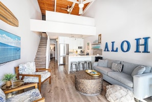 A spacious living area with a high ceiling, a kitchen with a central island, and a staircase leading to an upper level. - Maalaea Banyans 411 - Modern Renovation, Direct Ocean Front, Incredible View, AC (Wailuku)