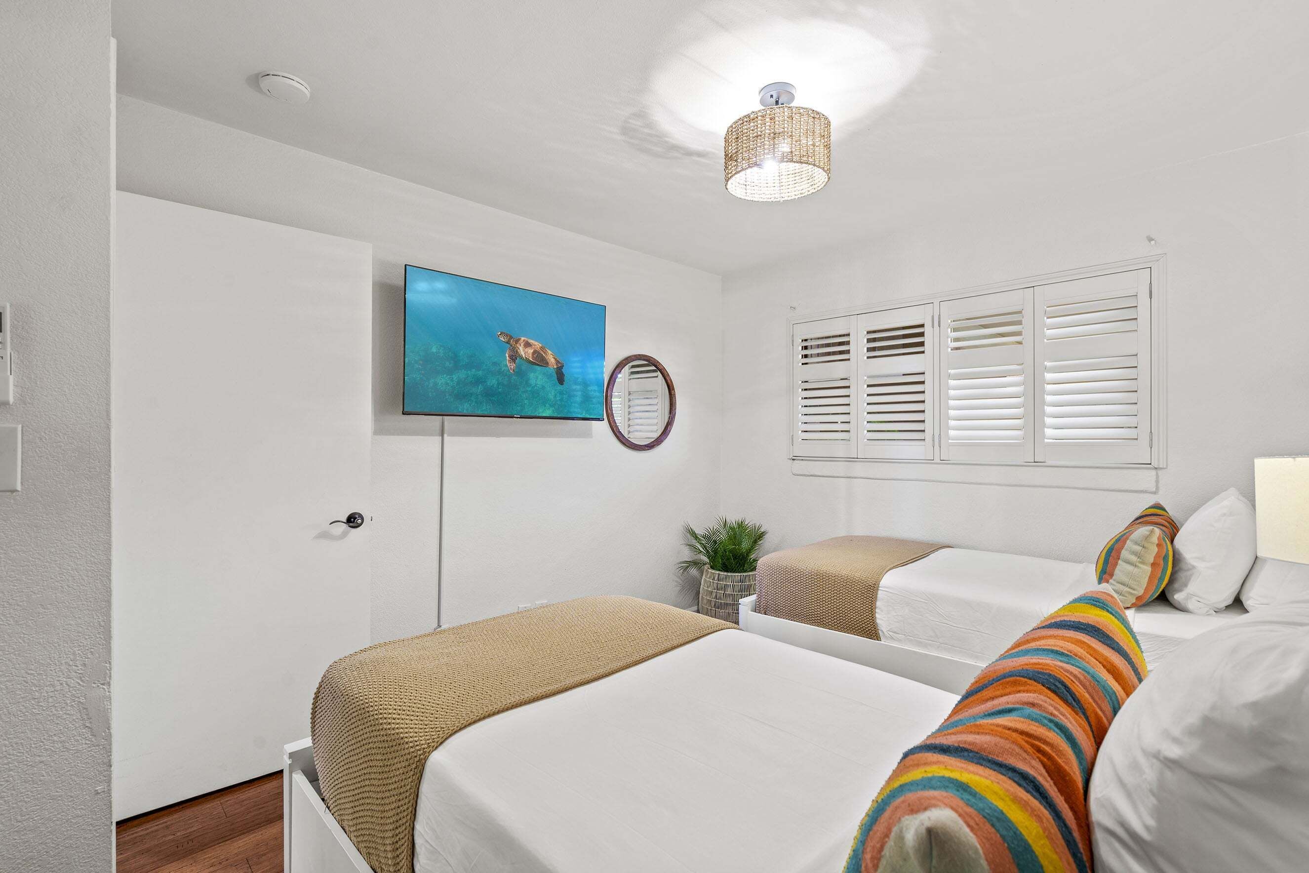 Habitación de hotel con dos camas, un televisor, una lámpara de techo y una ventana con persianas.