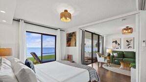 A bedroom with a large bed, a view of the sea, a green sofa, and a dining area with a table and chairs. - Oceanfront Lauloa 106 - Ground Floor, Modern Renovation, Split-ac, Walk to Beach (Wailuku)