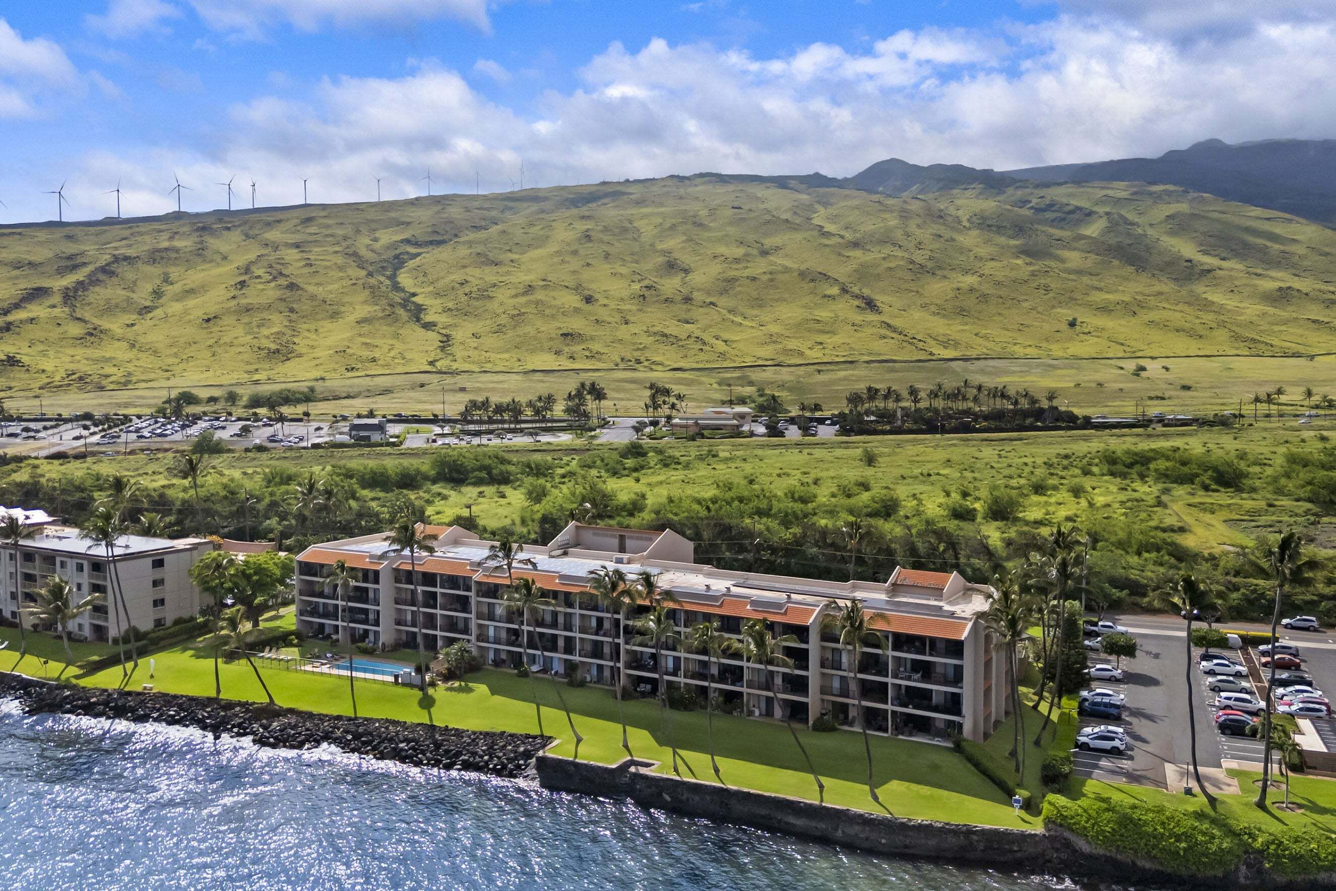 A hotel with multiple floors, a swimming pool, and a view of the ocean and hills.
