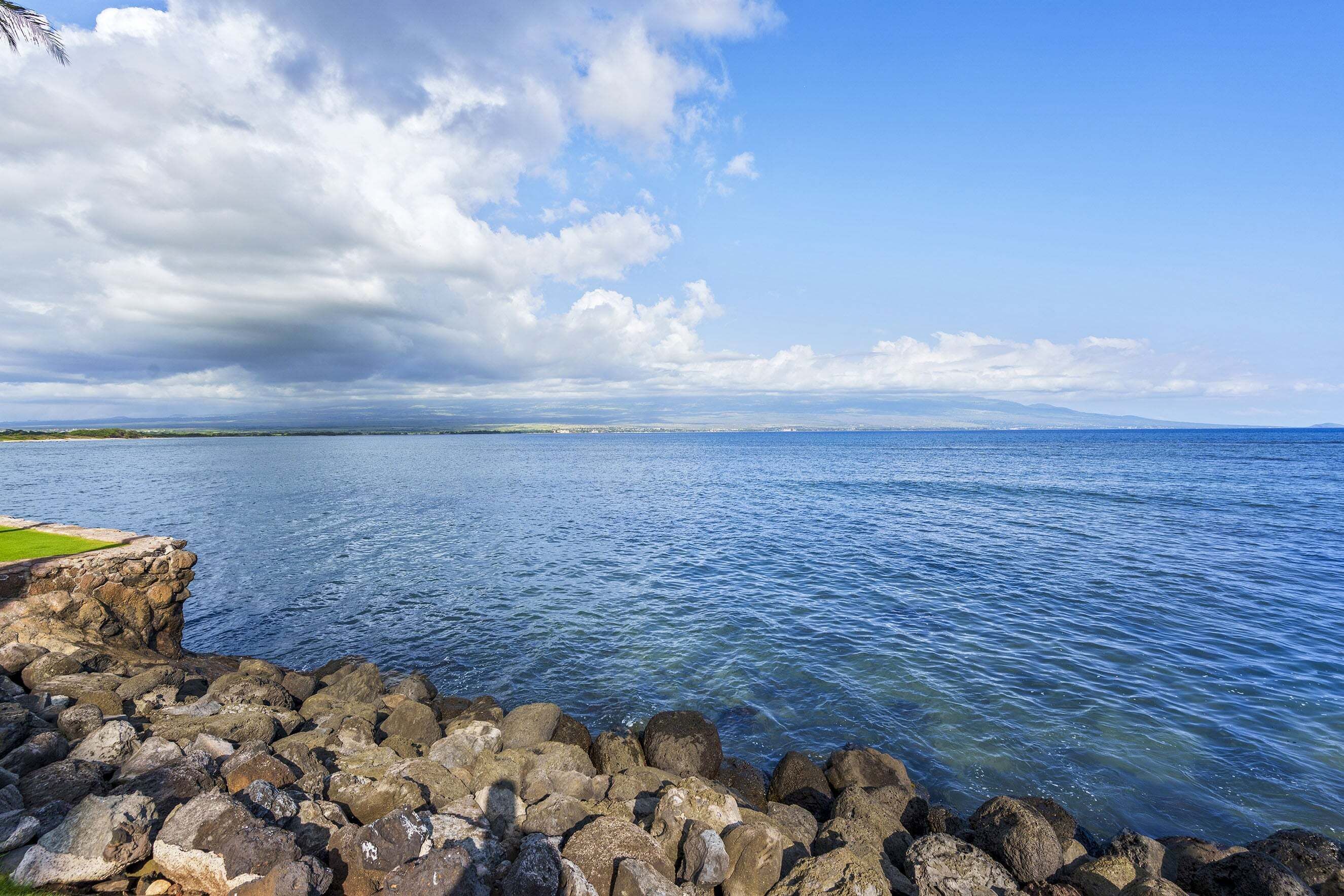 A rocky shoreline with clear blue water and a distant view of land.