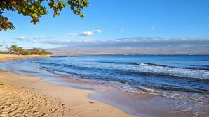 A beach with clear blue water, sandy shore, and distant mountains. - Oceanfront Lauloa 106 - Ground Floor, Modern Renovation, Split-ac, Walk to Beach (Wailuku)