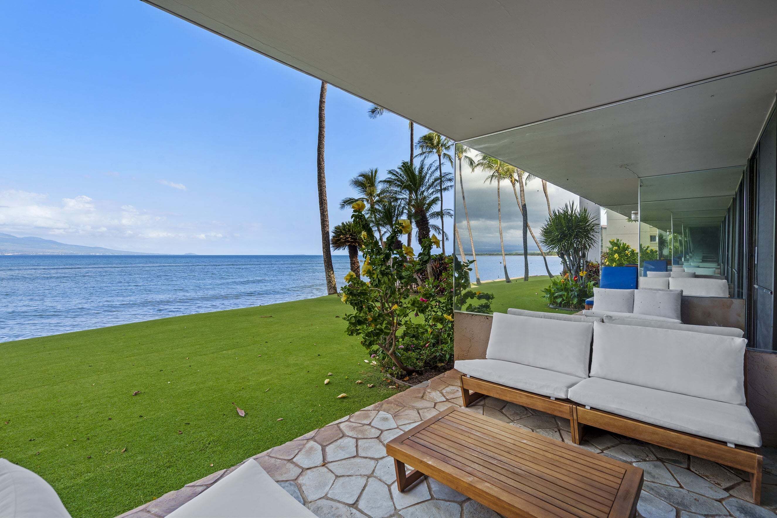 A patio with a view of the ocean, a grassy area, and a seating area with a table.