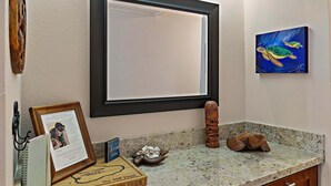 Un baño con encimera de granito, una fotografía enmarcada, una placa de madera y un cuadro de tortugas marinas.