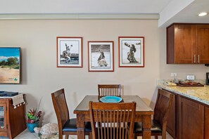 Ein Essbereich mit Holztisch und Stühlen, gerahmten Bildern an der Wand und einer Küchenzeile mit Schränken.