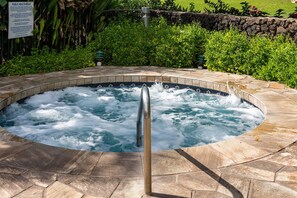 Un jacuzzi con barandilla de metal, rodeado de baldosas de piedra y abundante vegetación.
