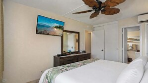 Habitación de hotel con cama, cómoda, ventilador de techo, un espejo grande y un cuadro de una playa.