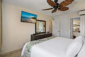 Ein Hotelzimmer mit einem Bett, einem Schminktisch, einem Deckenventilator, einem großen Spiegel und einem Gemälde mit Strandmotiv.