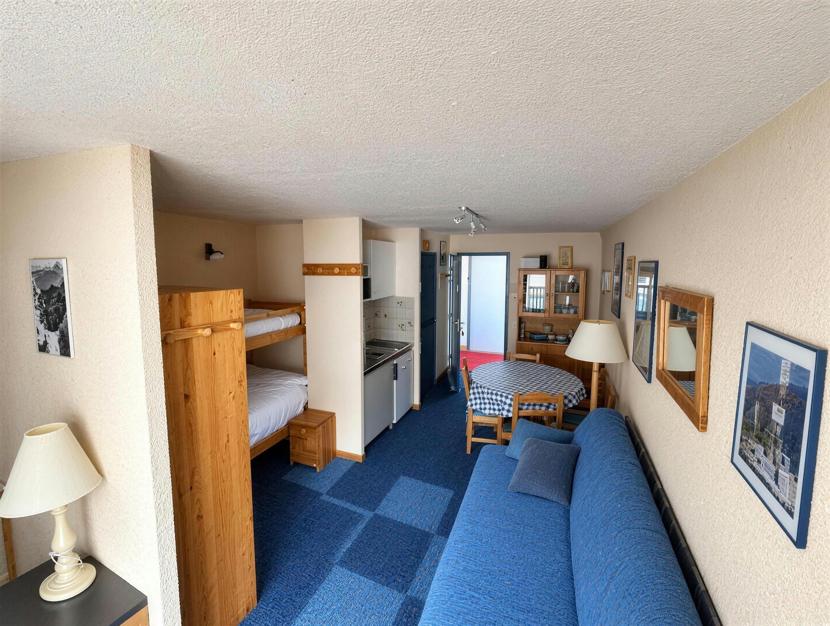 Ein kleines Zimmer mit Etagenbetten, einer Küchenzeile, einer Couch und einem Esstisch.