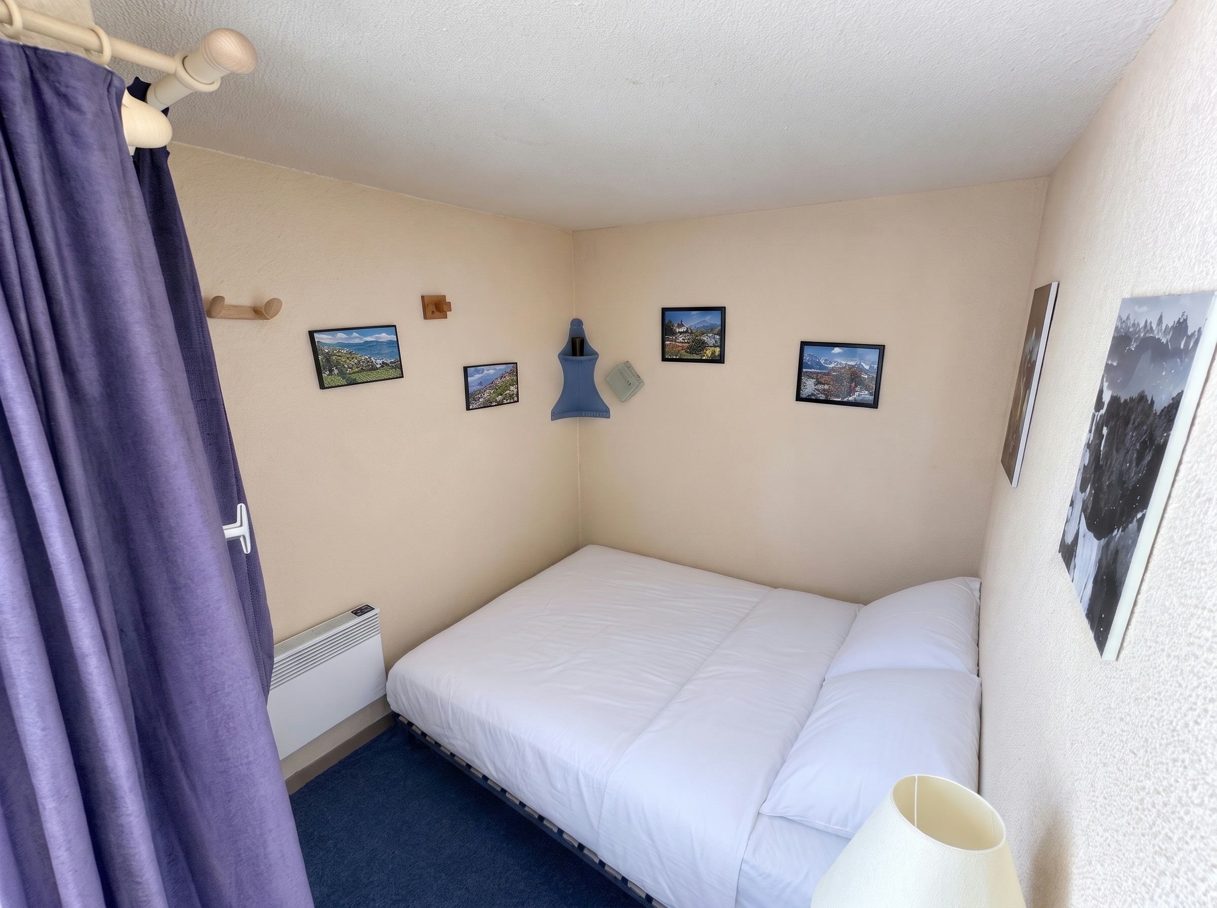 Un dormitorio con una cama individual, un radiador, una ventana con cortinas y cuatro cuadros enmarcados en la pared.
