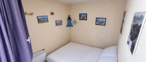 Un dormitorio con una cama individual, un radiador, una ventana con cortinas y cuatro cuadros enmarcados en la pared.