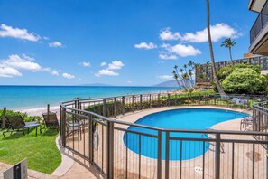 Piscina com vista para o oceano e uma praia, cercada por palmeiras e um edifício.
