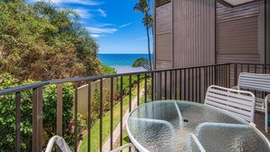 A balcony with a glass table and chairs, overlooking a beach and ocean. - Hale Hui Kai 208 - Ocean View Luxury Condo on the Best Beach on Maui, Split AC! (Kihei)